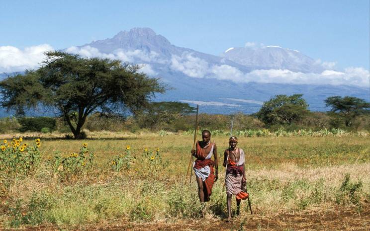Maasai people walking through the landscape beneath Kilimanjaro